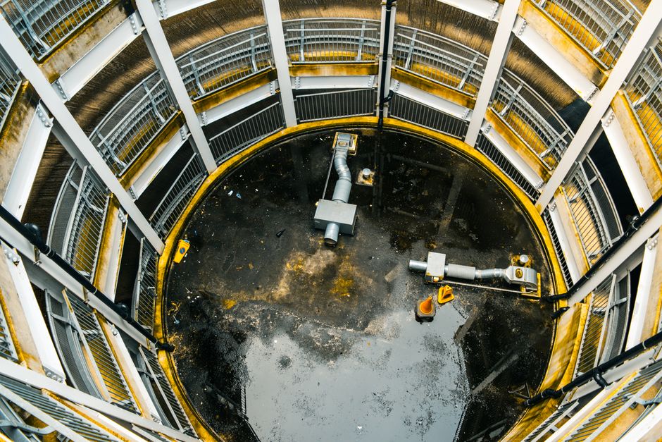 An underground basement area featuring a tiled floor with a dark matte finish and a smooth surface, illuminated by natural light filtering in from an unseen source. In the background, a metal staircas